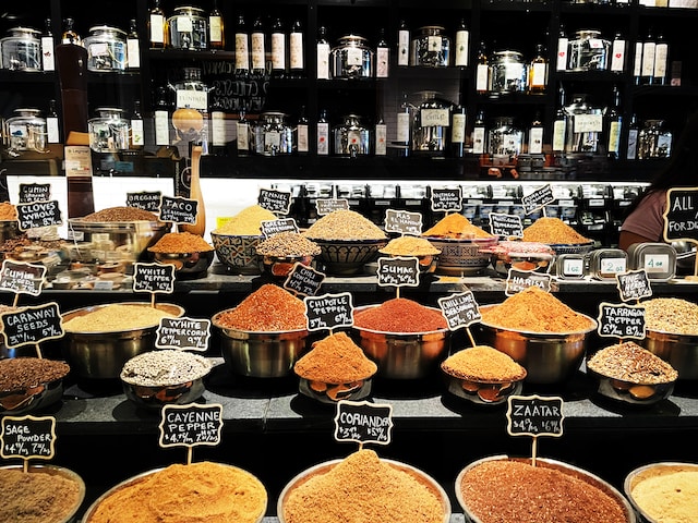 A variety of spices are displayed in large bowls with signs indicating their names and prices